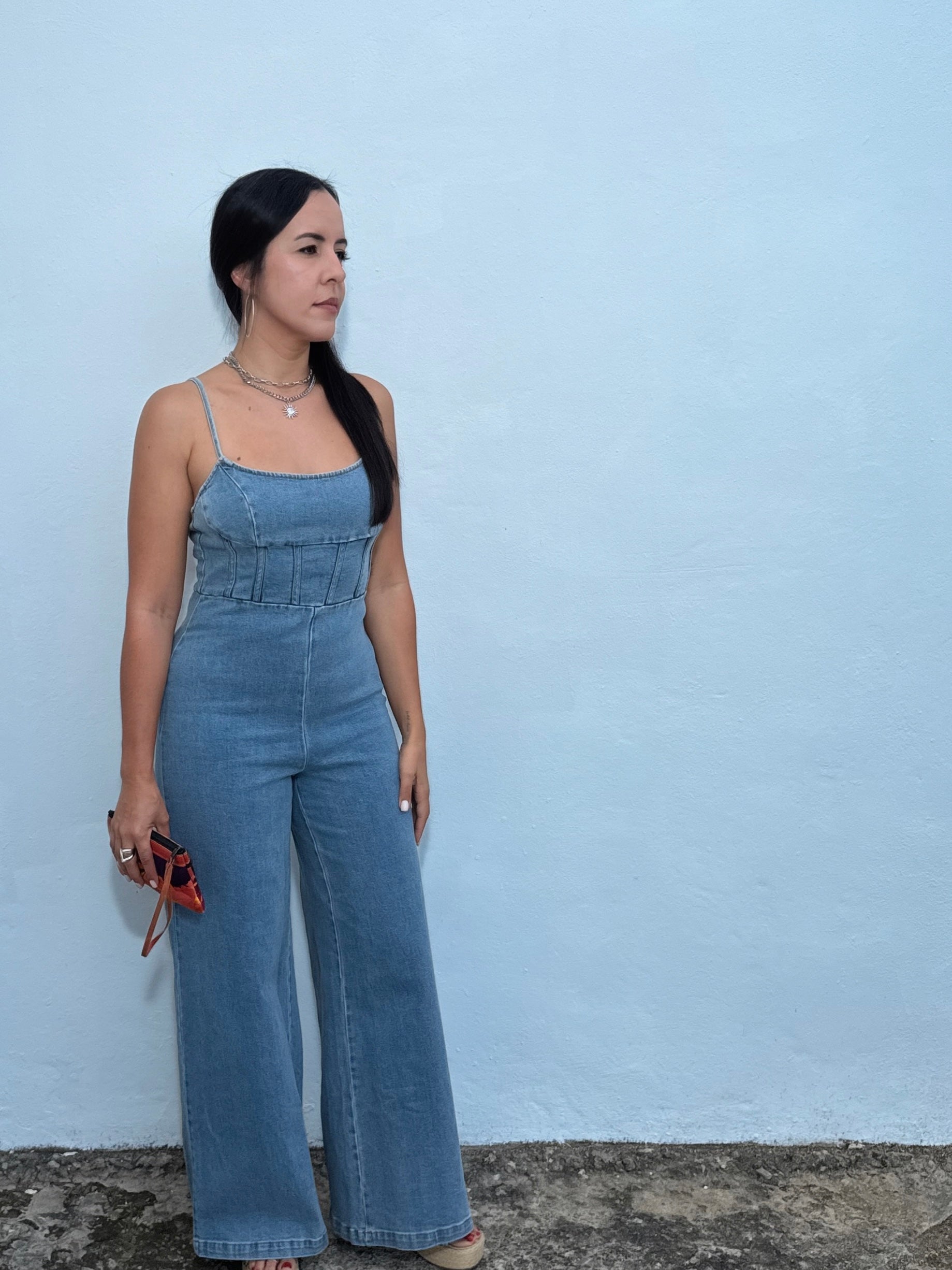 Woman wearing a denim jumpsuit against a light blue wall.